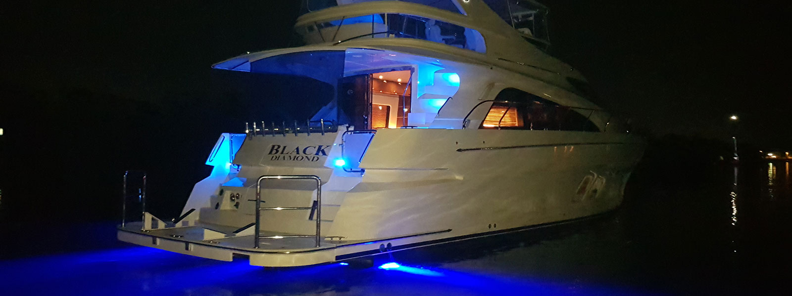 Yacht at night with blue lighting in water.